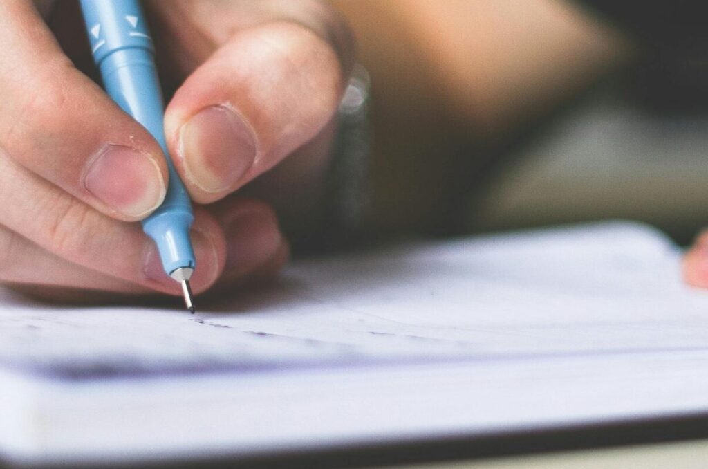 Close-up of hand writing in notebook using a blue pen, focus on creativity.