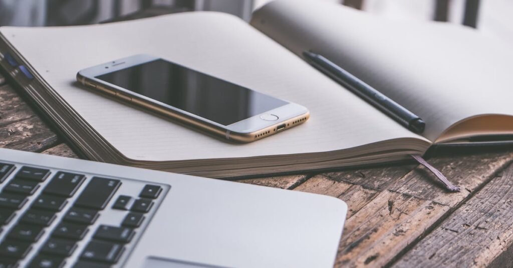 Open notebook with a smartphone and laptop on a wooden desk, creating a contemporary workspace vibe.